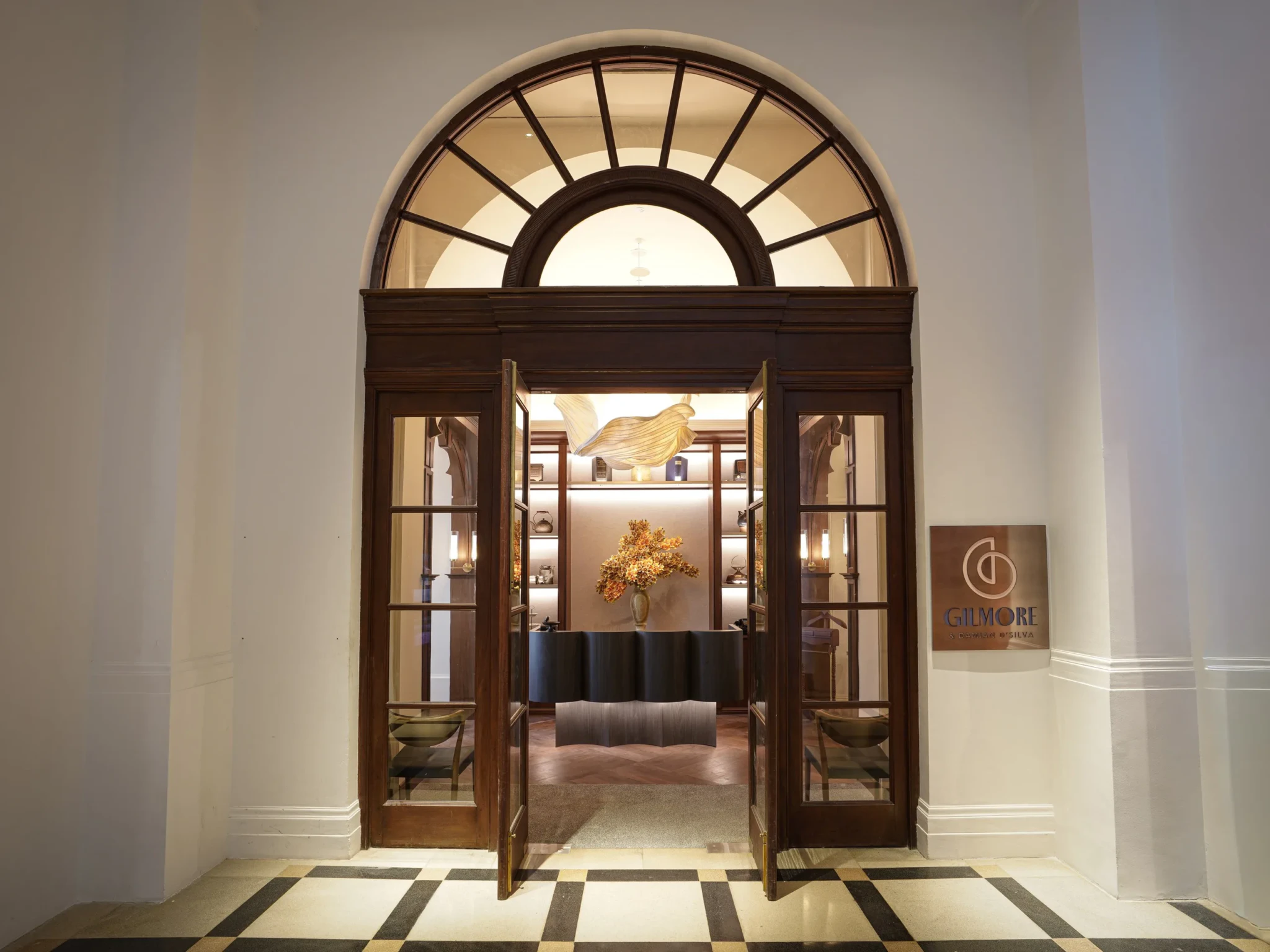 The storefront entrance to Gilmore restaurant with wooden doors, fanlight window, and sculptural art installations visible inside.