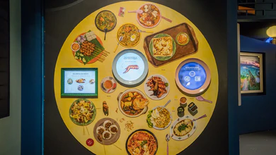 Colourful hawker dishes arranged on a bright yellow interactive table in the Singapore History Gallery
