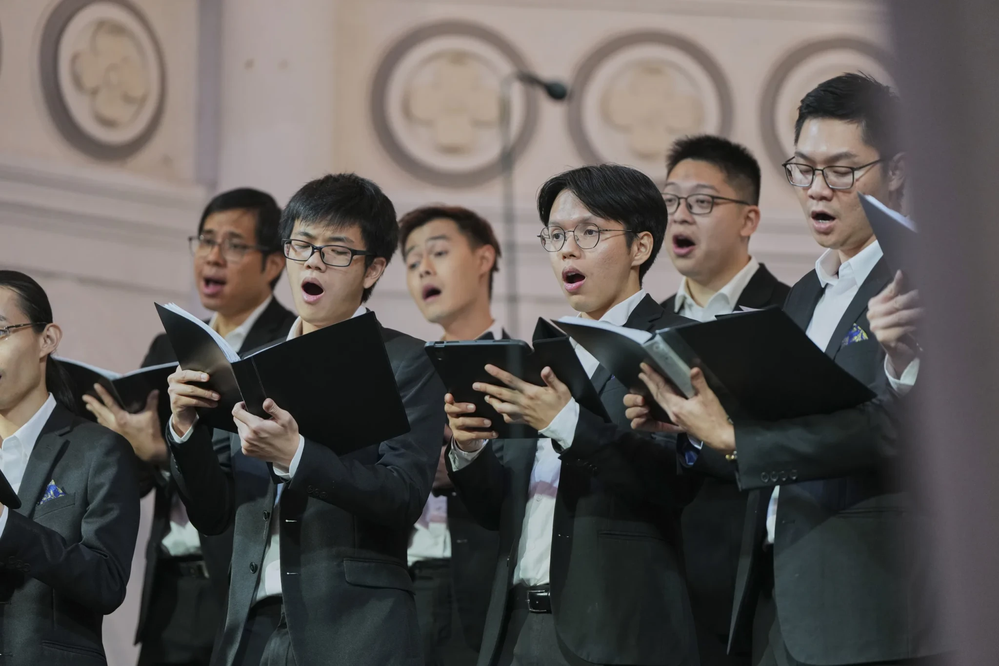 Members of VOS Men singing in formal attire with sheet music in hand