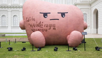 Large pink cartoon-like sculpture with downturned eyes on museum lawn