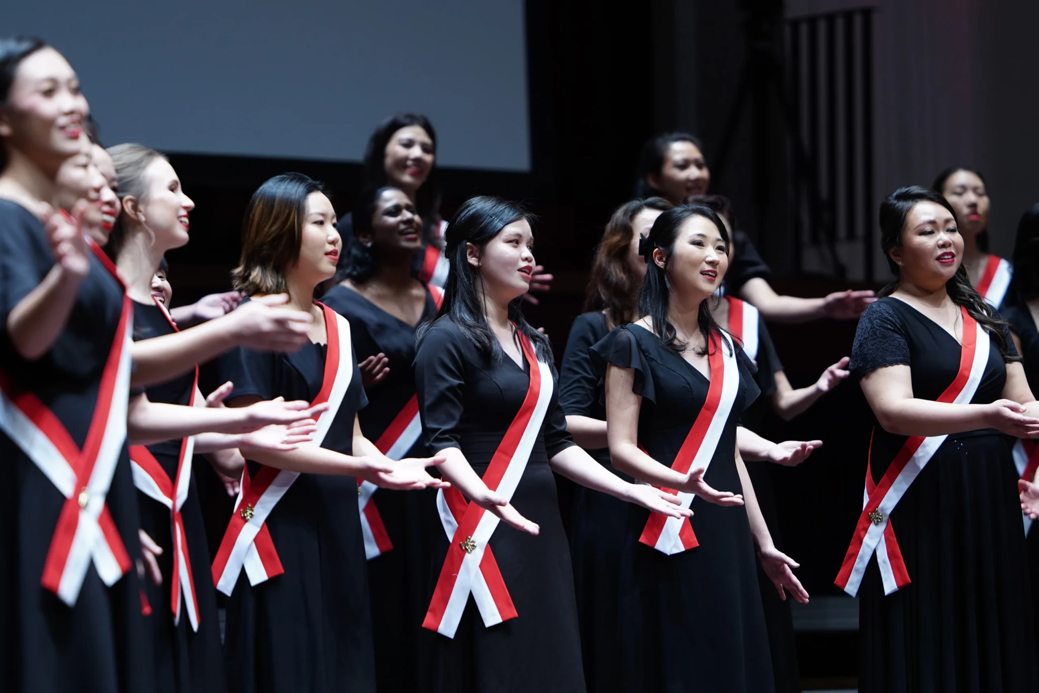 The VOS Ladies Choir performing in black outfits with red and white sashes at SOTA Concert Hall