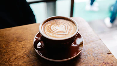 A latte with heart-shaped latte art in a brown cup on a wooden café table