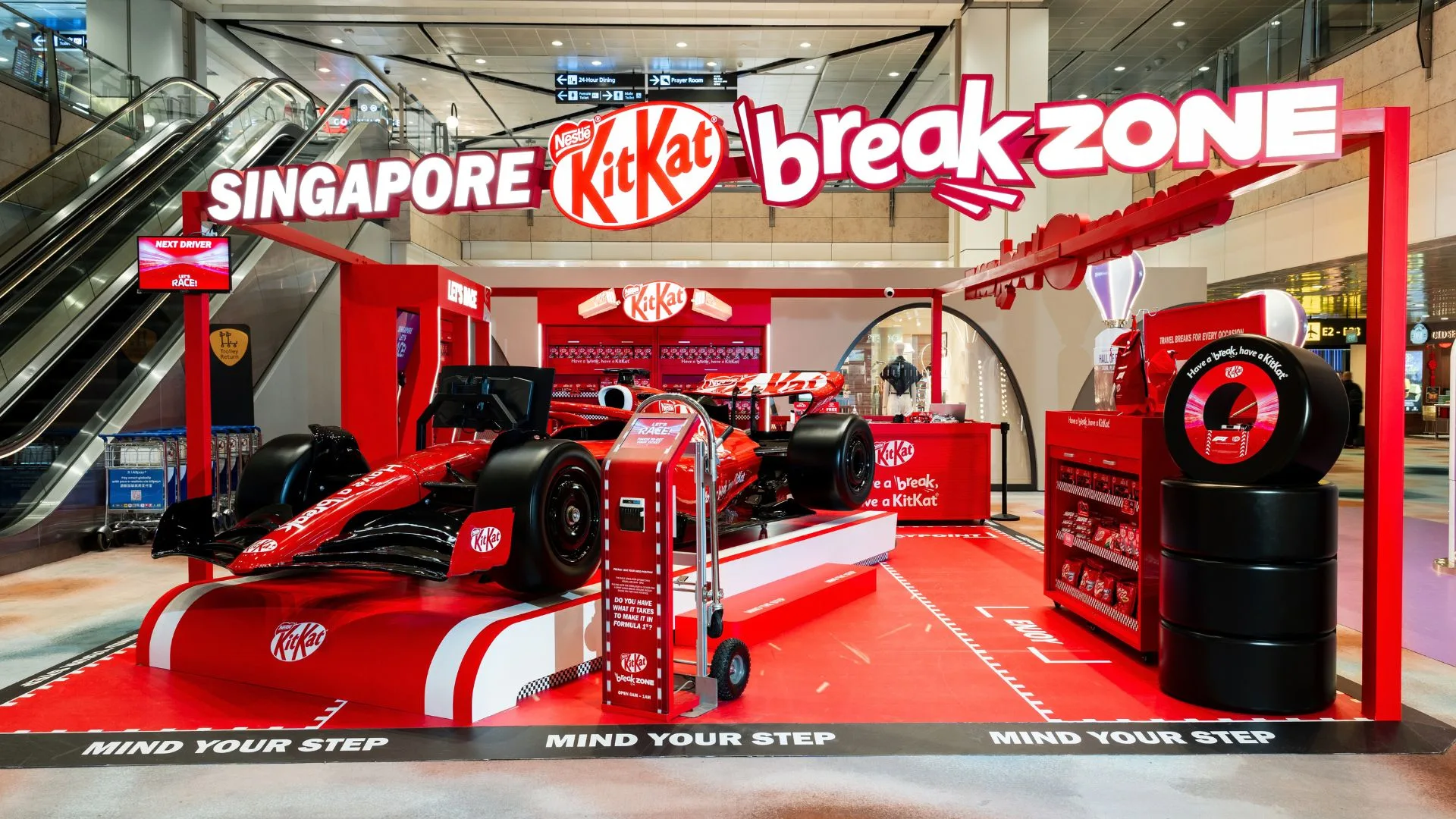 Red KitKat-branded Formula 1 racing zone at Changi Airport with simulator car and racing tire display