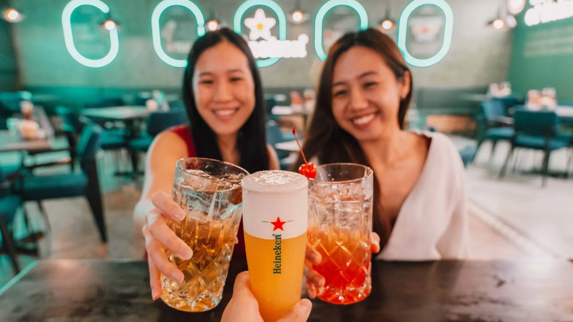 Two women toast at the neon-lit Heineken World Bar