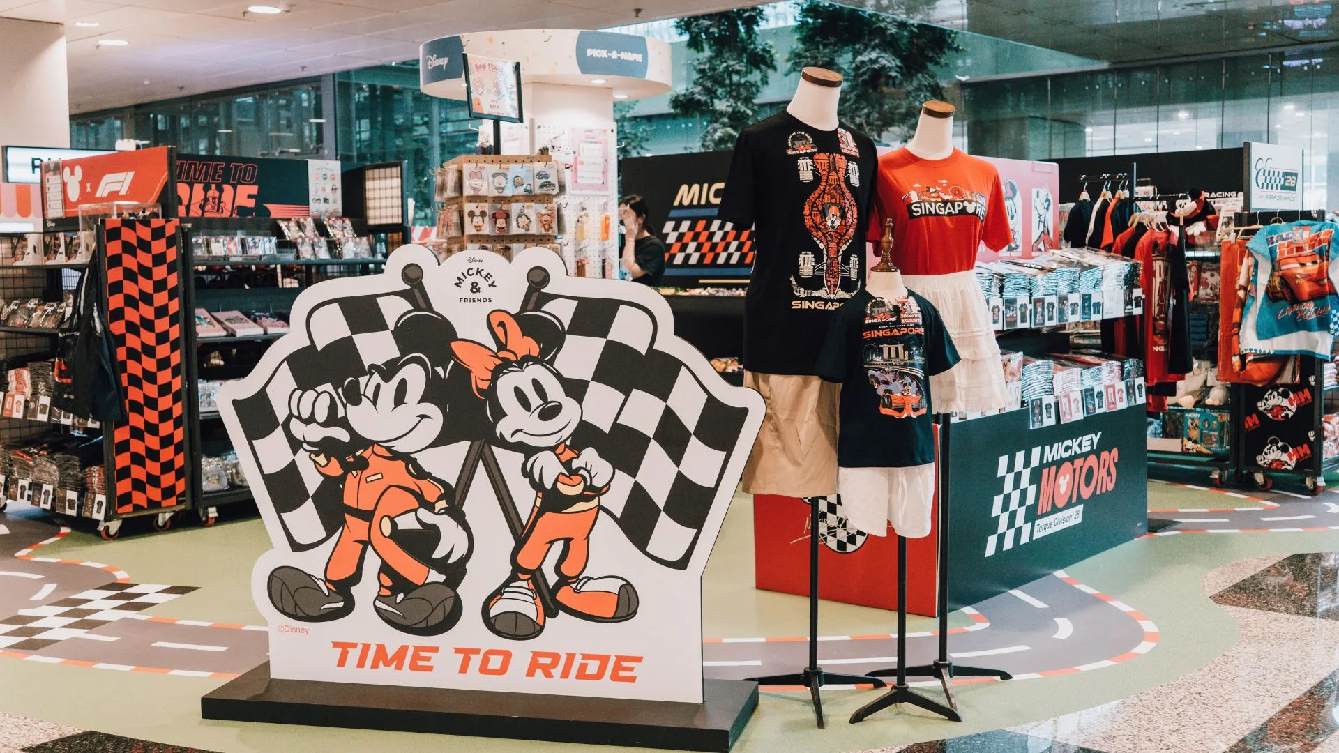 Mickey and Minnie Mouse in orange racing suits holding a checkered flag at a pop-up store display