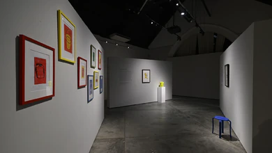 Interior of Held in the Middle at Objectifs with framed linocut prints on white walls and a blue stool on the floor