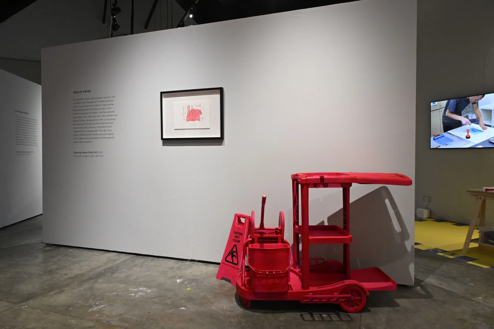 A red cleaning cart displayed in the gallery space of Held in the Middle