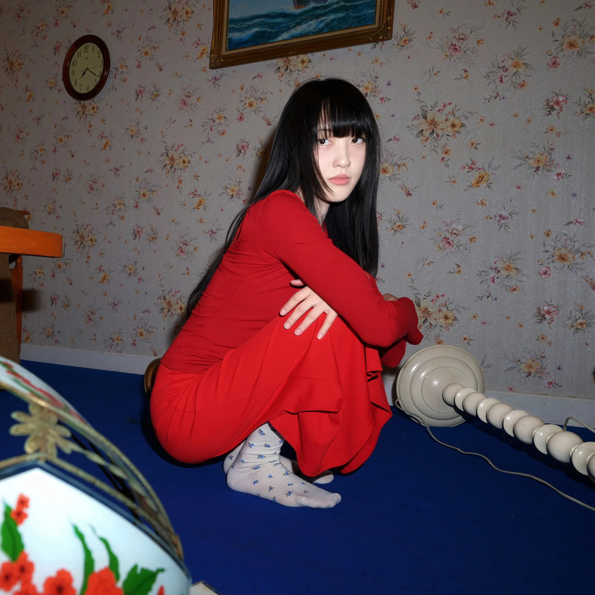 pami in a red jacket against floral wallpaper with a vintage clock behind her