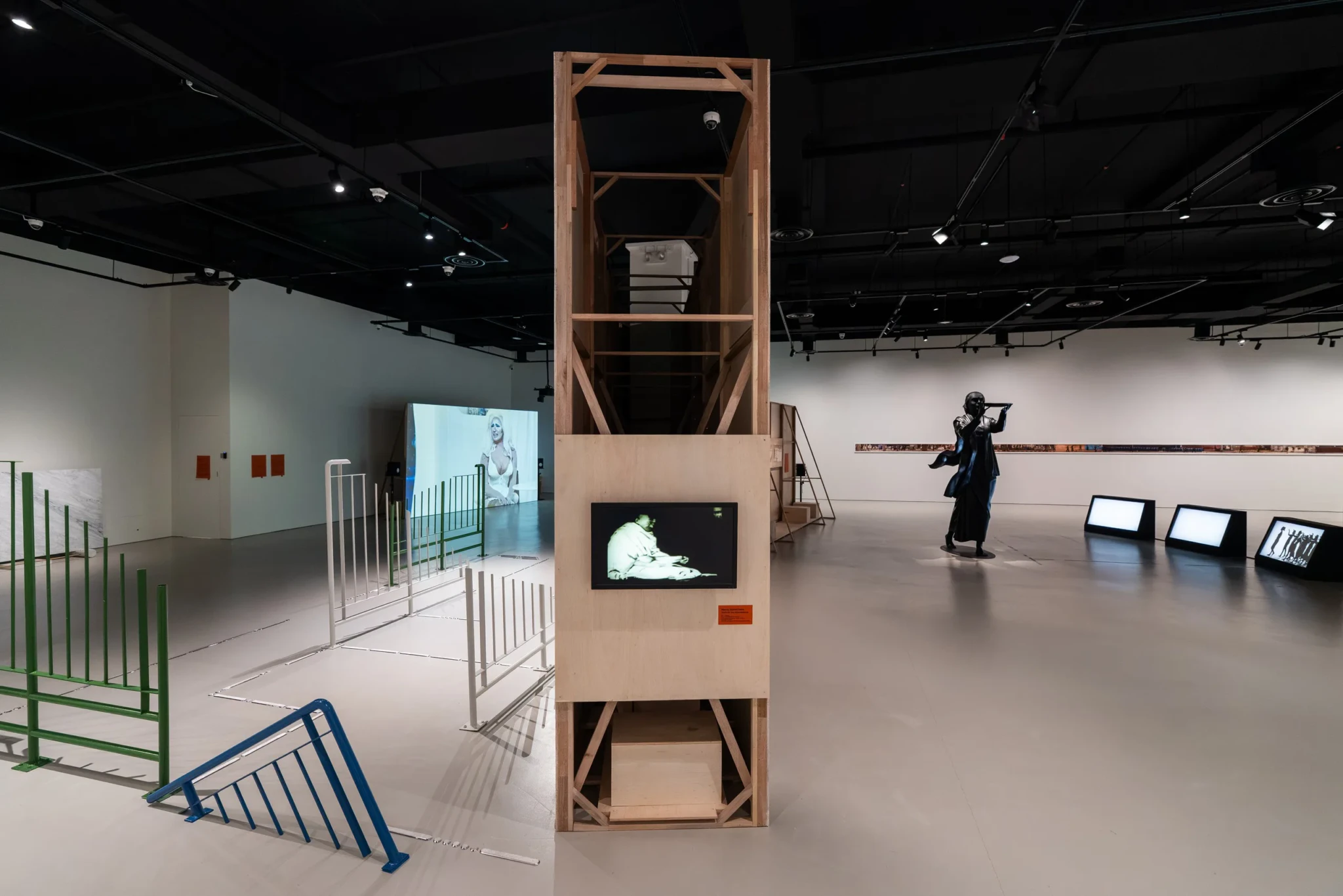 Exhibition view of SAMCollection: The Present is Unstable with a tall wooden structure, video displays and metal barriers