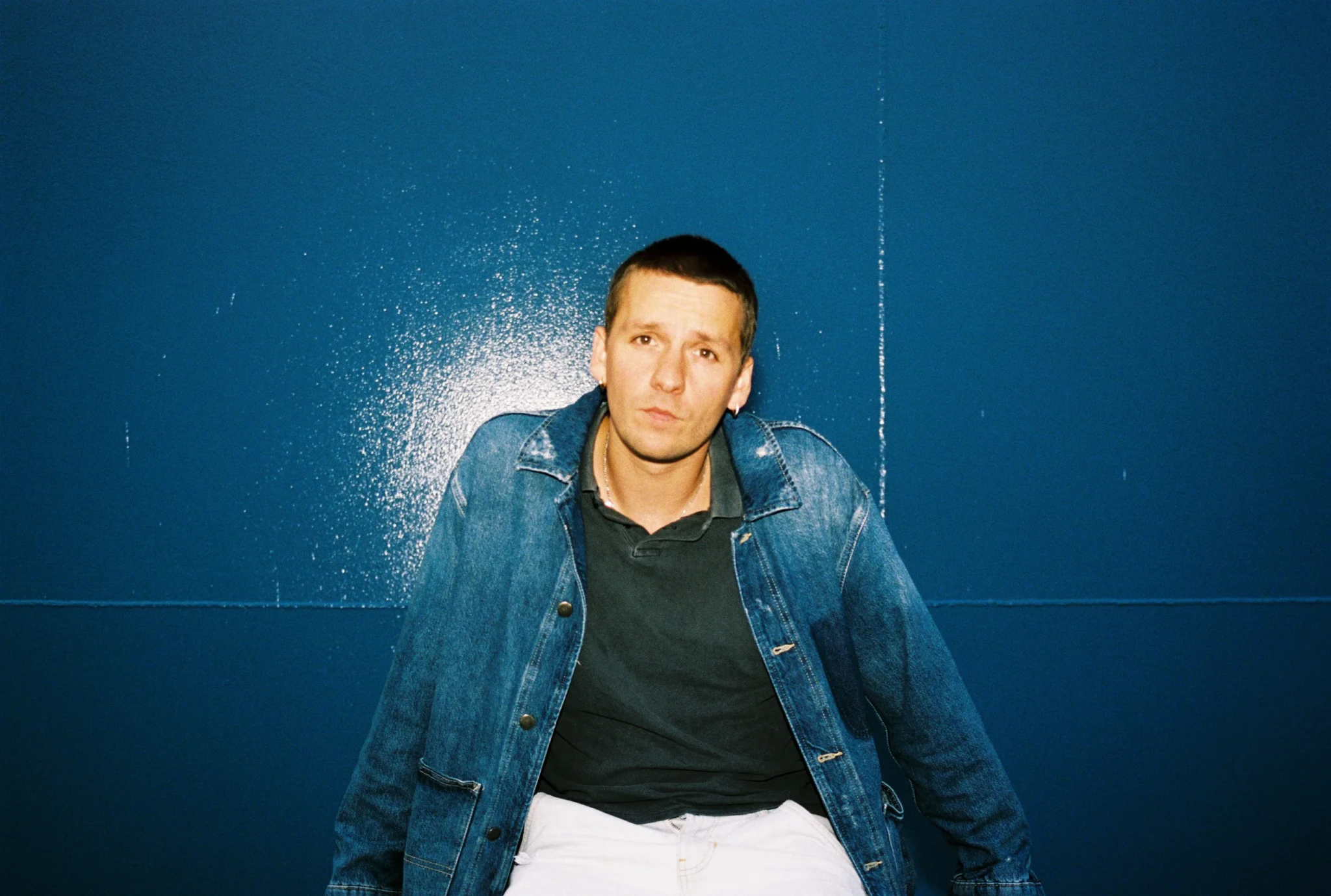 Oliver Symons in a press portrait against a blue background