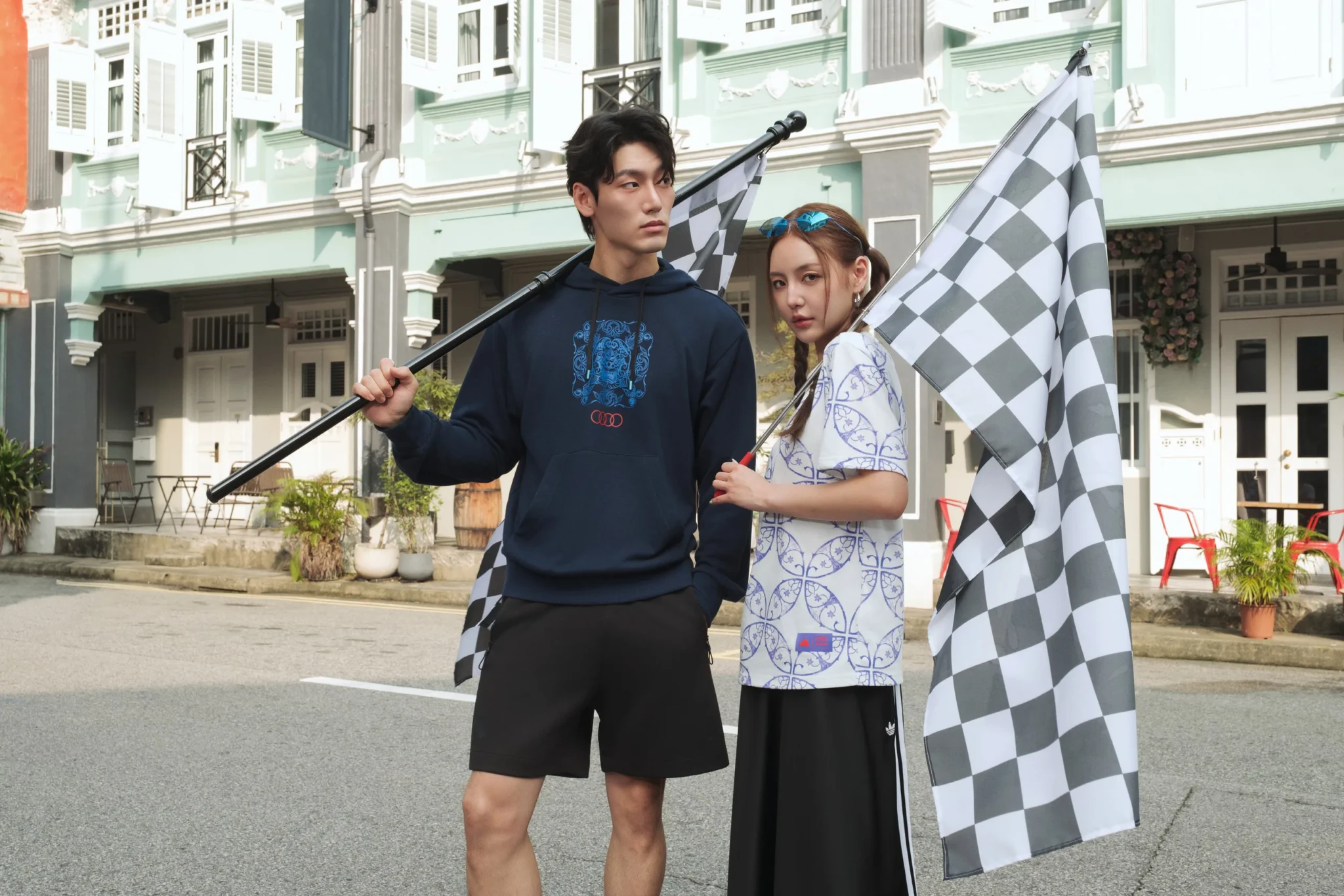Two people holding a large checkered flag in front of colonial architecture at Funan