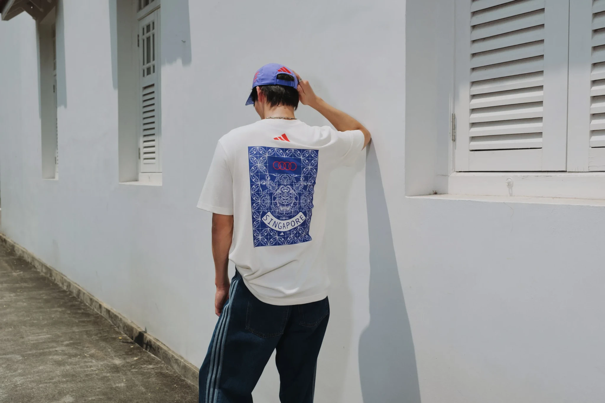 Person from behind wearing adidas x Audi F1 Team Singapore t-shirt and cap in white corridor