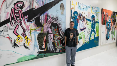 Danny Minnick standing in his Los Angeles studio in front of large, colourful canvases