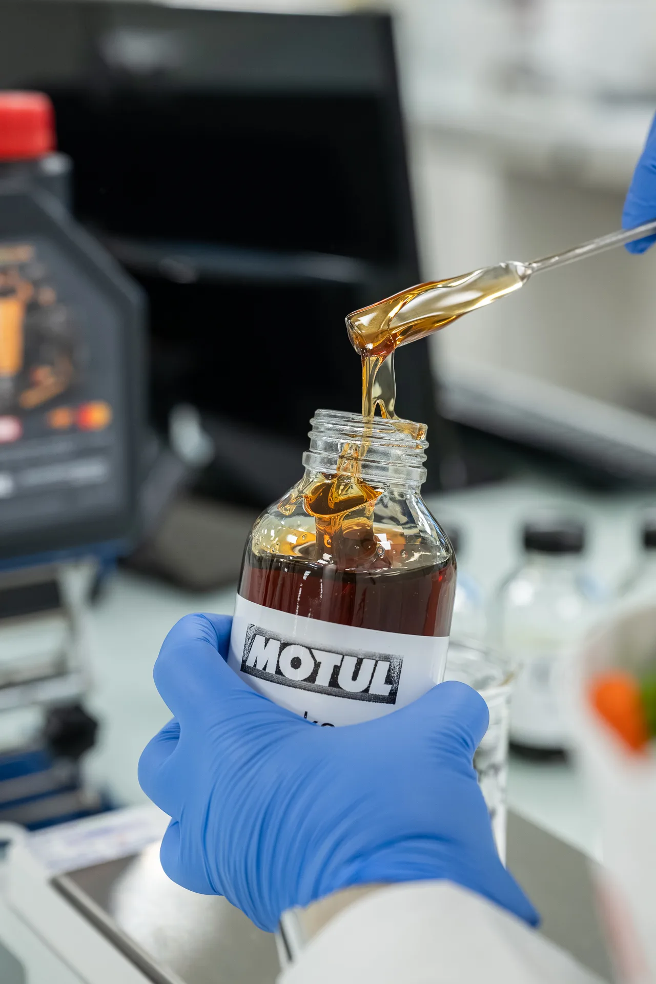 Gloved hand dispensing Motul 2714E gear oil into a sample bottle