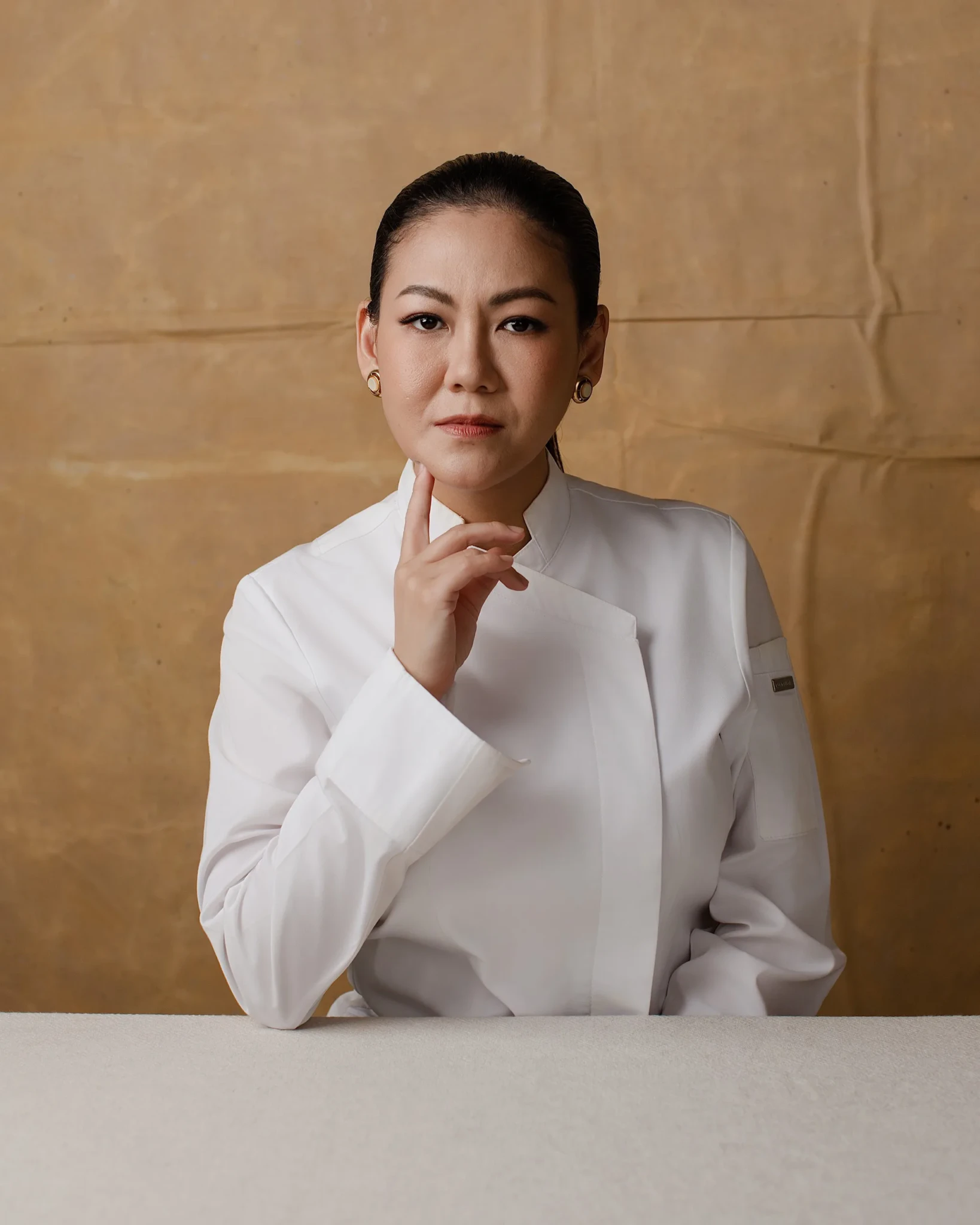 Chef Johanne Siy in a white chef's coat against a textured tan background