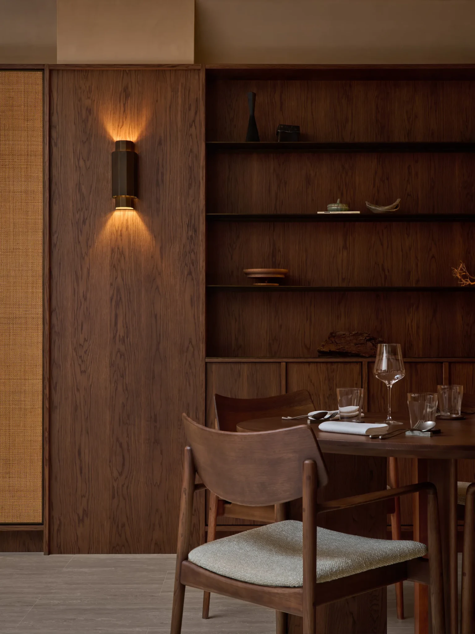 A wooden dining chair with a cream fabric seat at a wooden table set with glassware