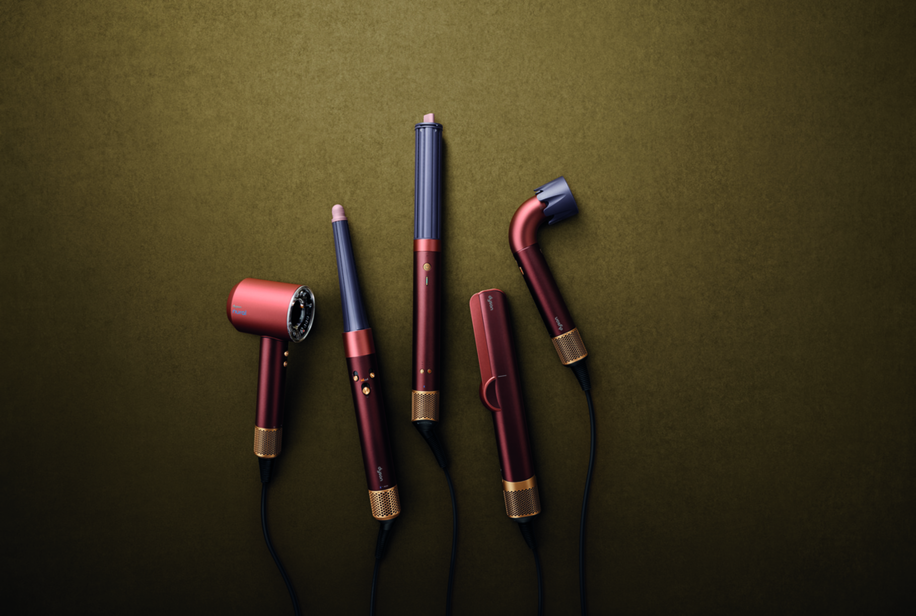 Five Dyson hair care devices in the Plum and Copper colourway arranged flat against a warm olive background
