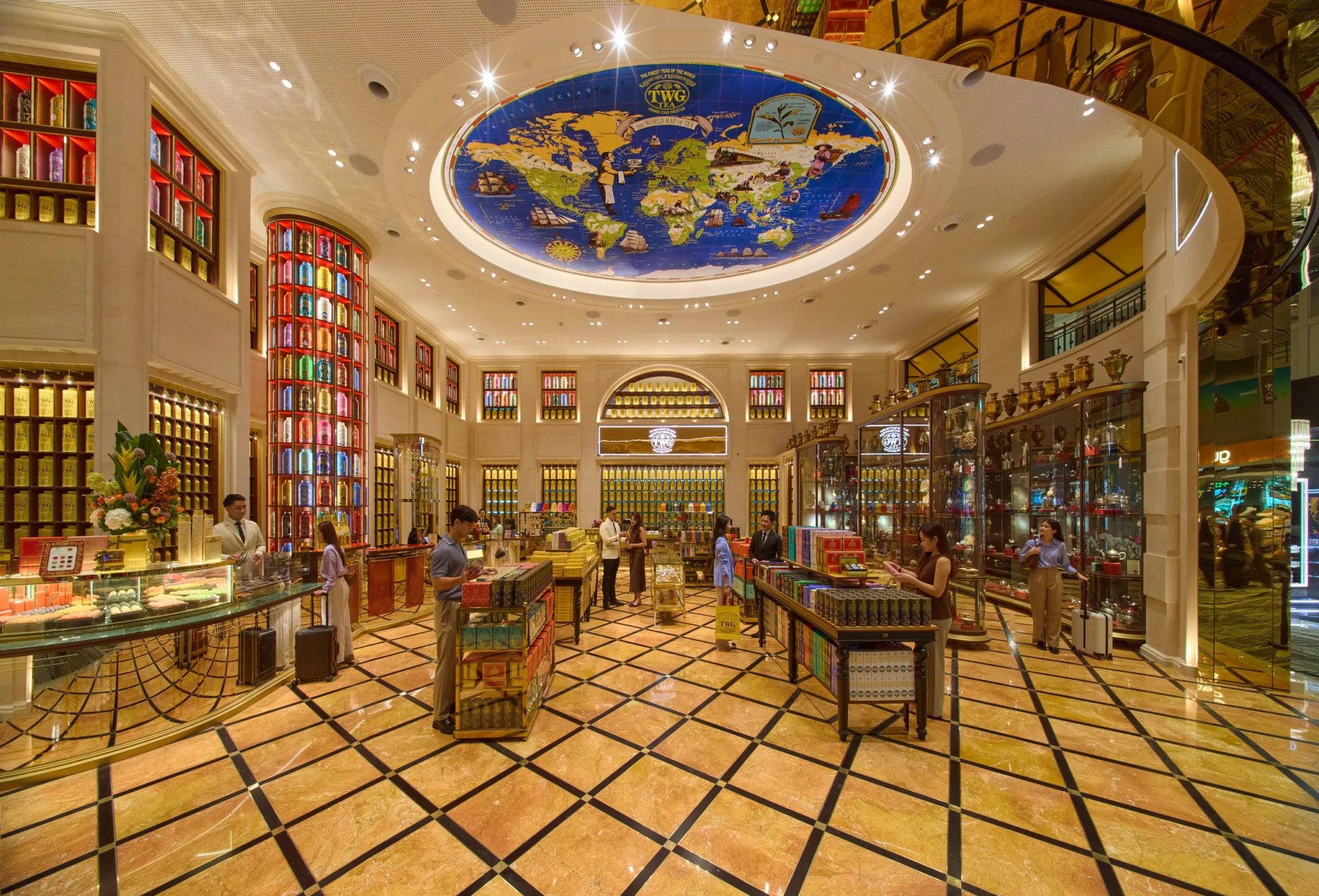 Interior of TWG Tea Gallery showing ornate ceiling with world map, red-framed display cases, and polished marble flooring