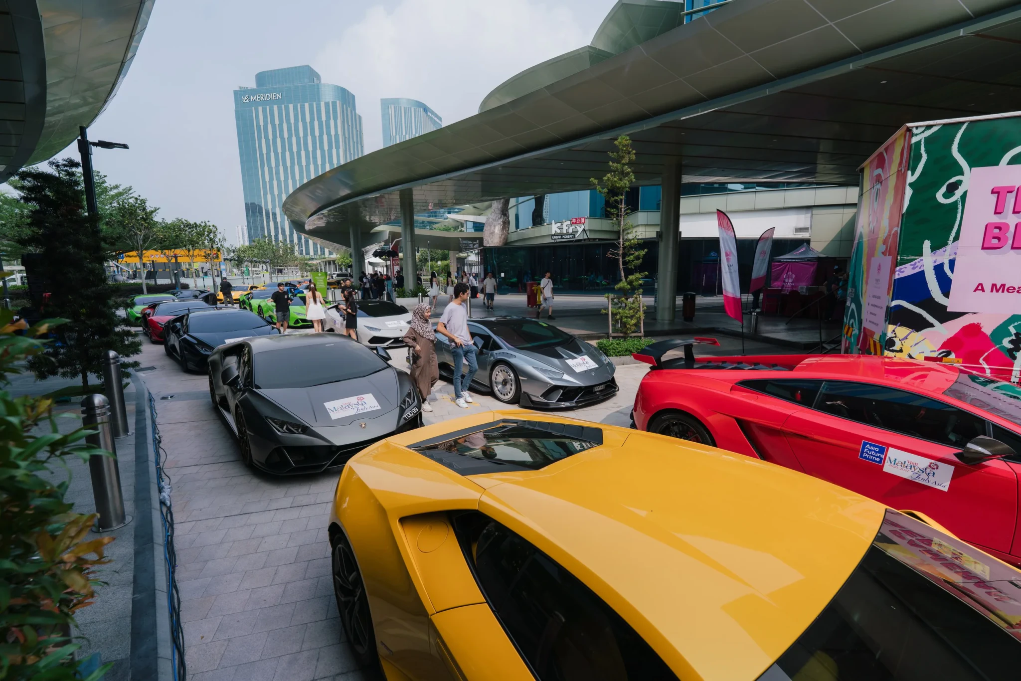 Yellow, black and red Lamborghinis displayed at an outdoor automotive event under a highway overpass