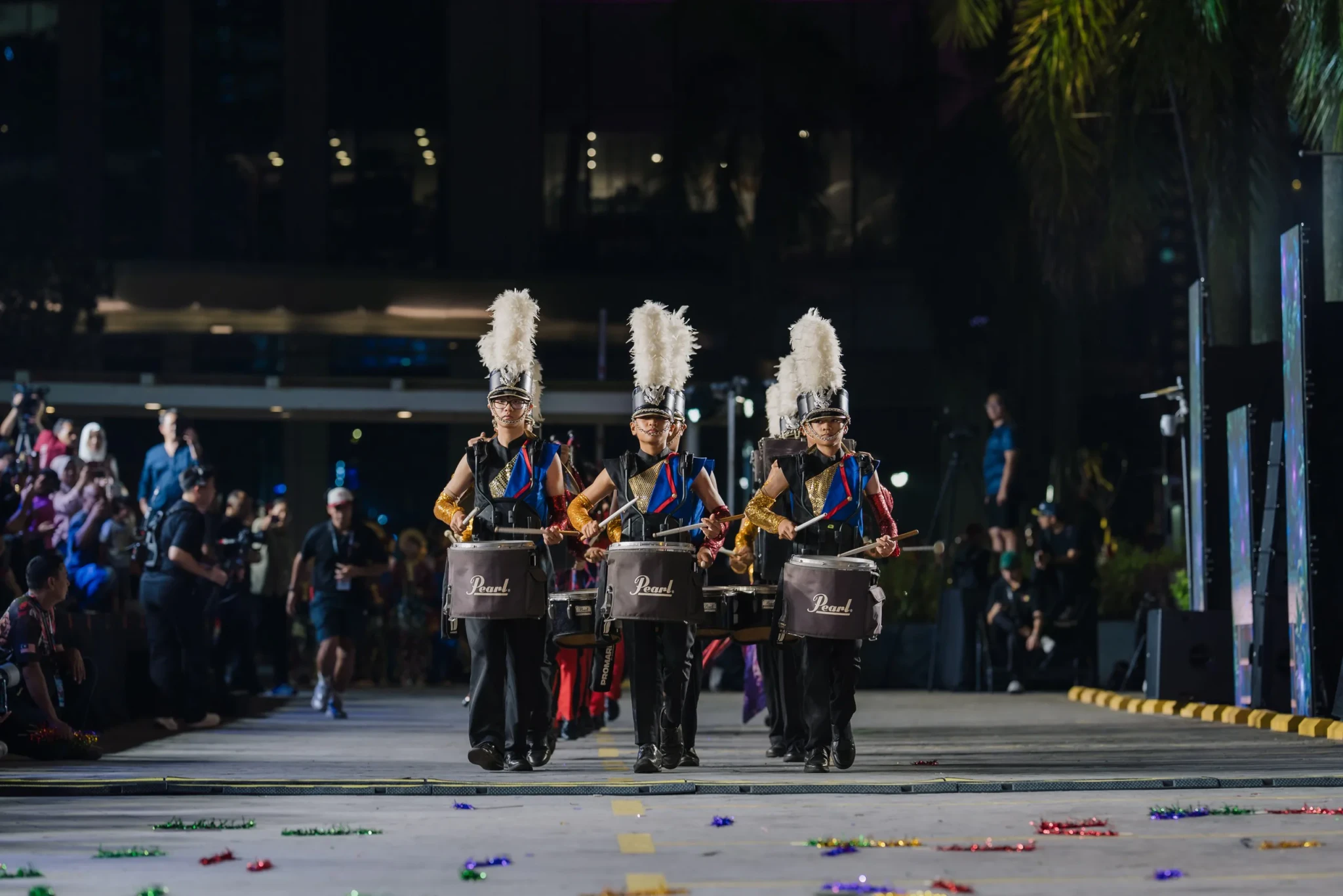 Three drummers in tall white feathered headdresses and gold-trimmed black uniforms playing during the Colours of Parade