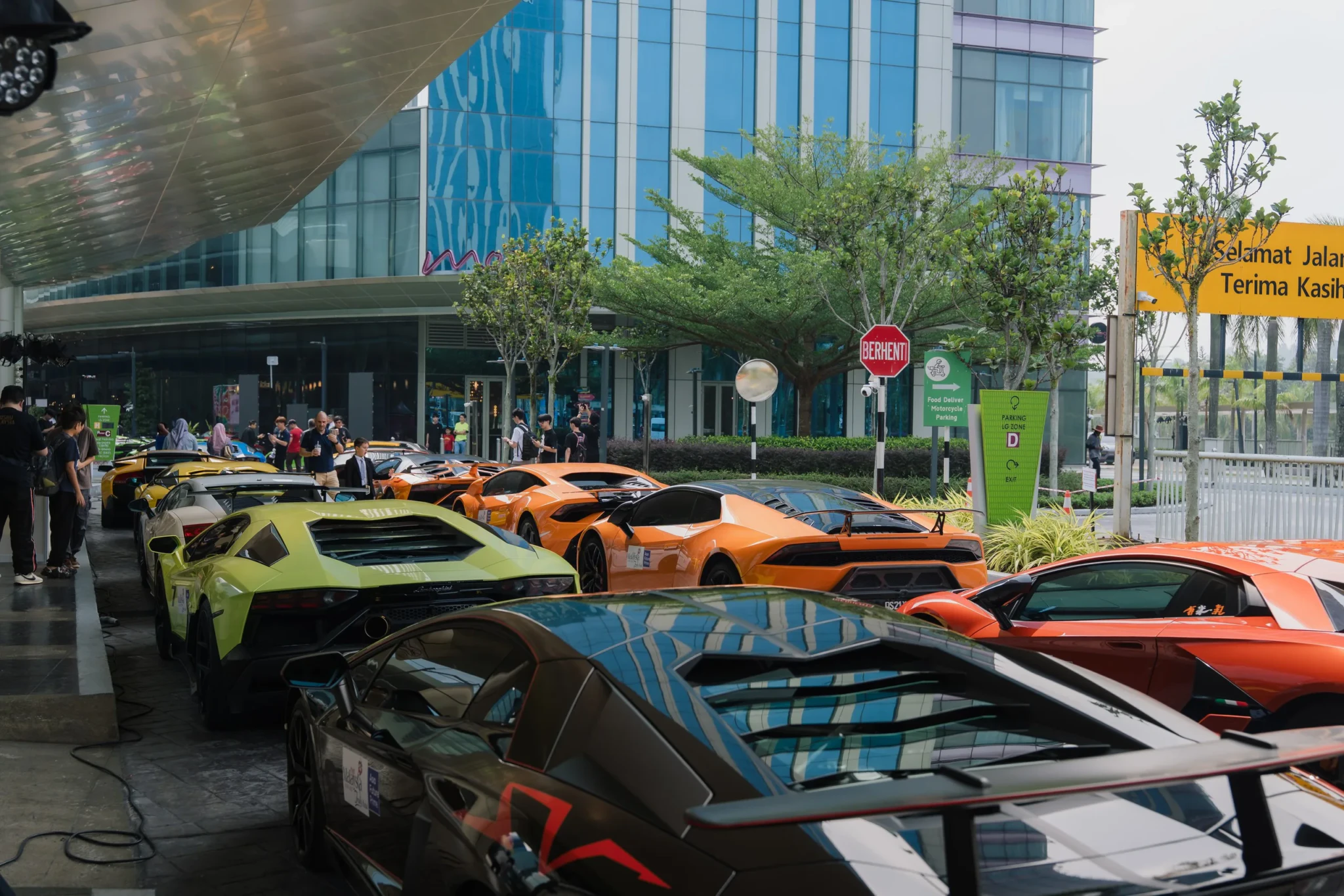Lamborghinis in lime green, orange and red lined up in front of a modern glass building with street-level vendors
