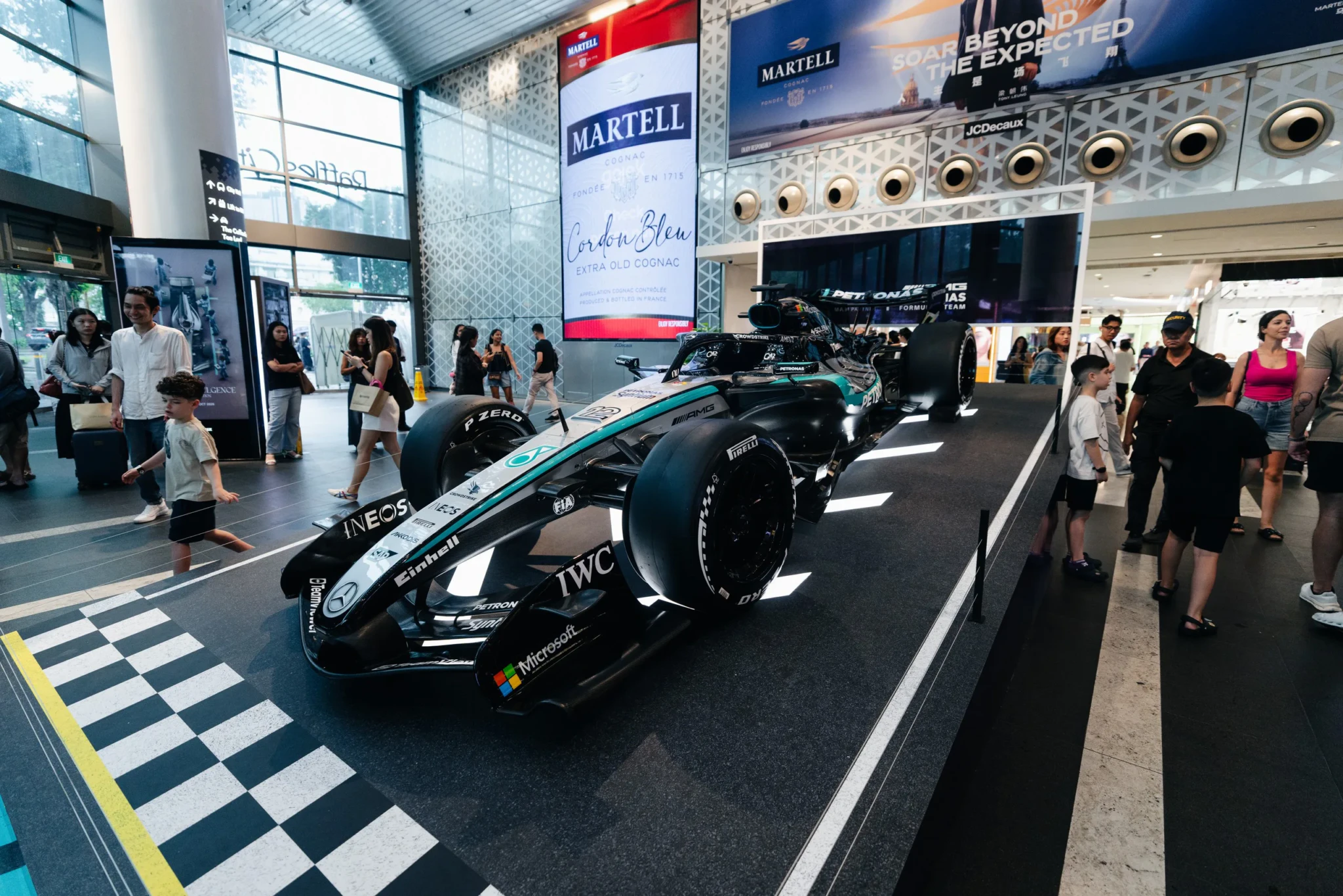 Formula 1 race car with turquoise and black livery displayed indoors at a shopping mall with visitors around it