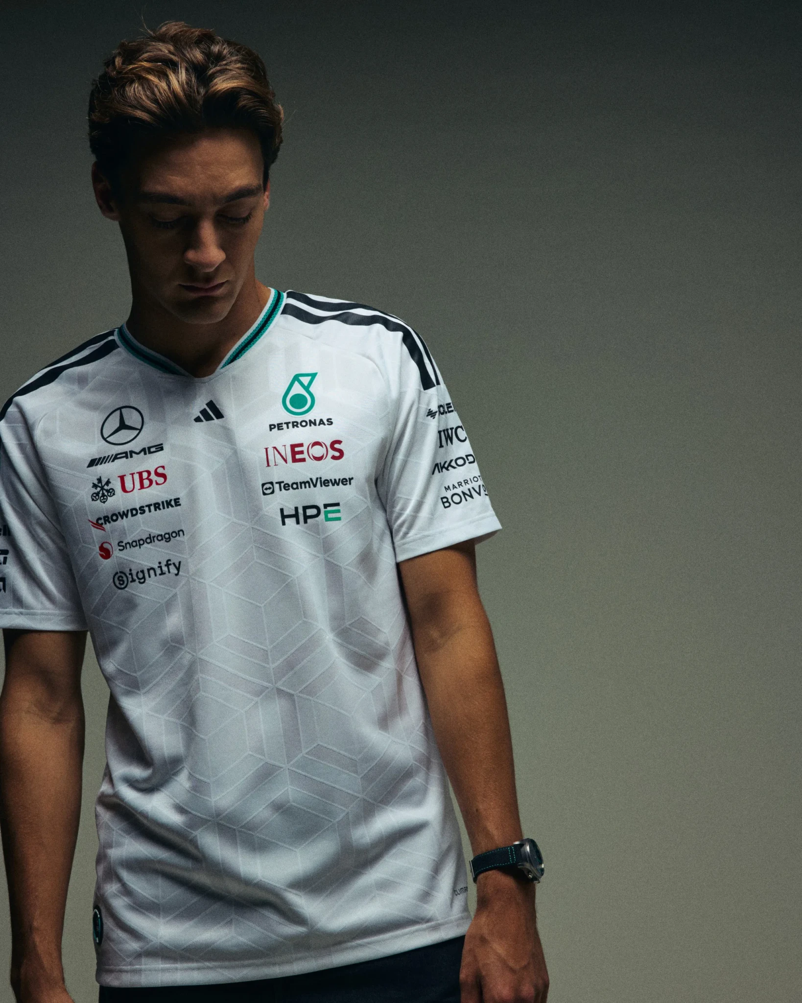A model in the white adidas x Mercedes-AMG PETRONAS F1 Team jersey with Petronas, INEOS, TeamViewer, and HPE logos
