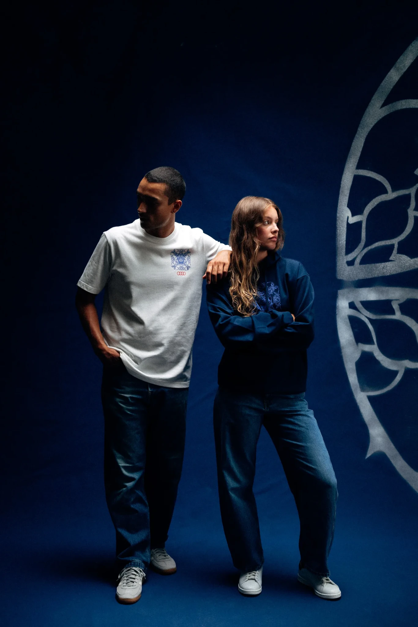 Two people in branded casualwear against a deep blue background with geometric pattern