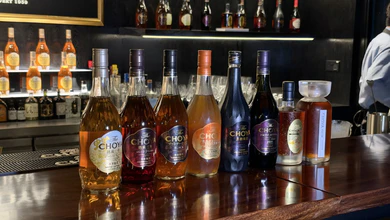 A row of CHOYA ume liqueur bottles, from pale to dark, lined up on the bar counter at The CHOYA Ginza BAR Singapore