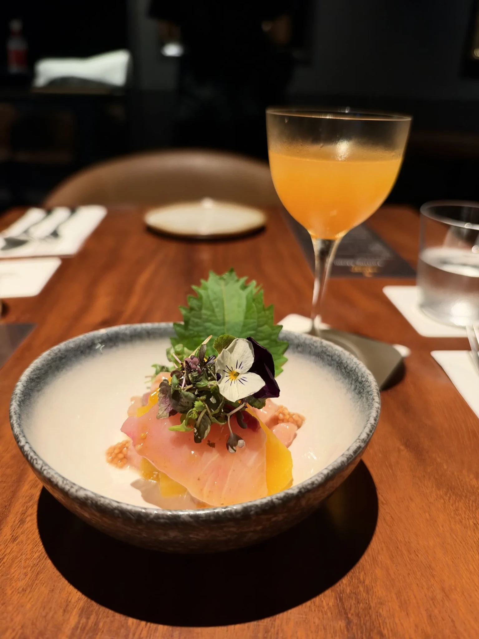 Plated cured fish with garnish and a golden cocktail on a dining table