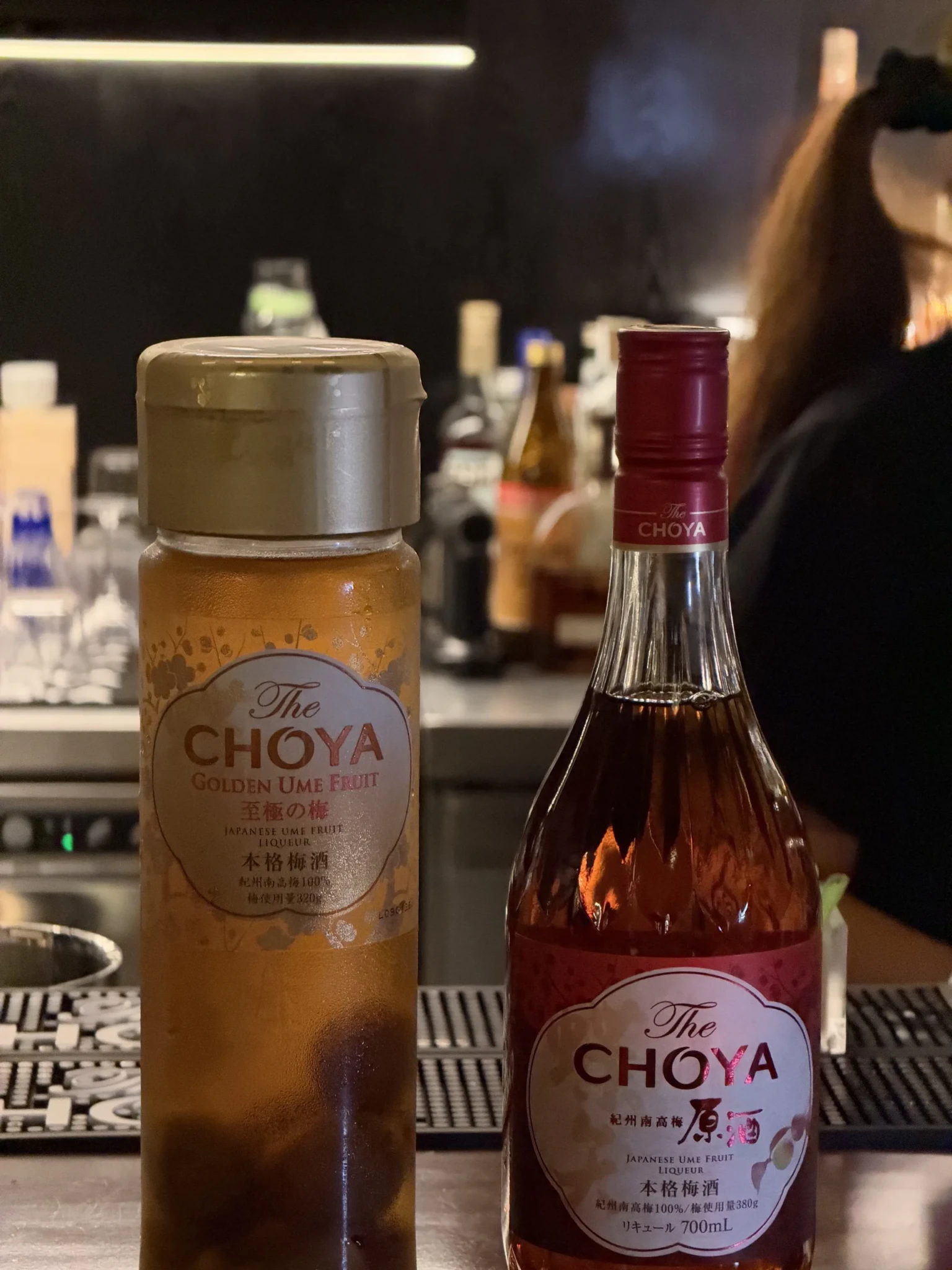 Two CHOYA ume liqueur bottles displayed at a bar counter