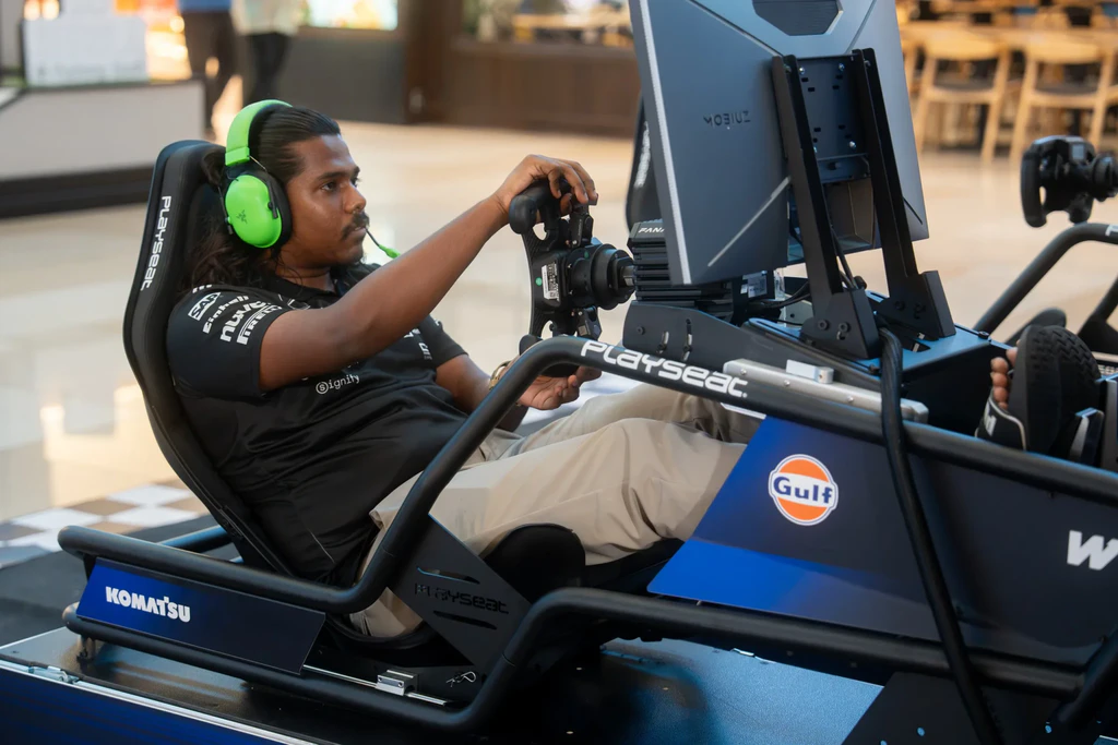 A participant in neon green Razer headphones steering a Williams-branded race car simulator at New Era Bugis Junction