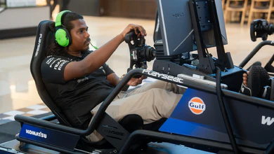 A participant in neon green Razer headphones steering a Williams-branded race car simulator at New Era Bugis Junction
