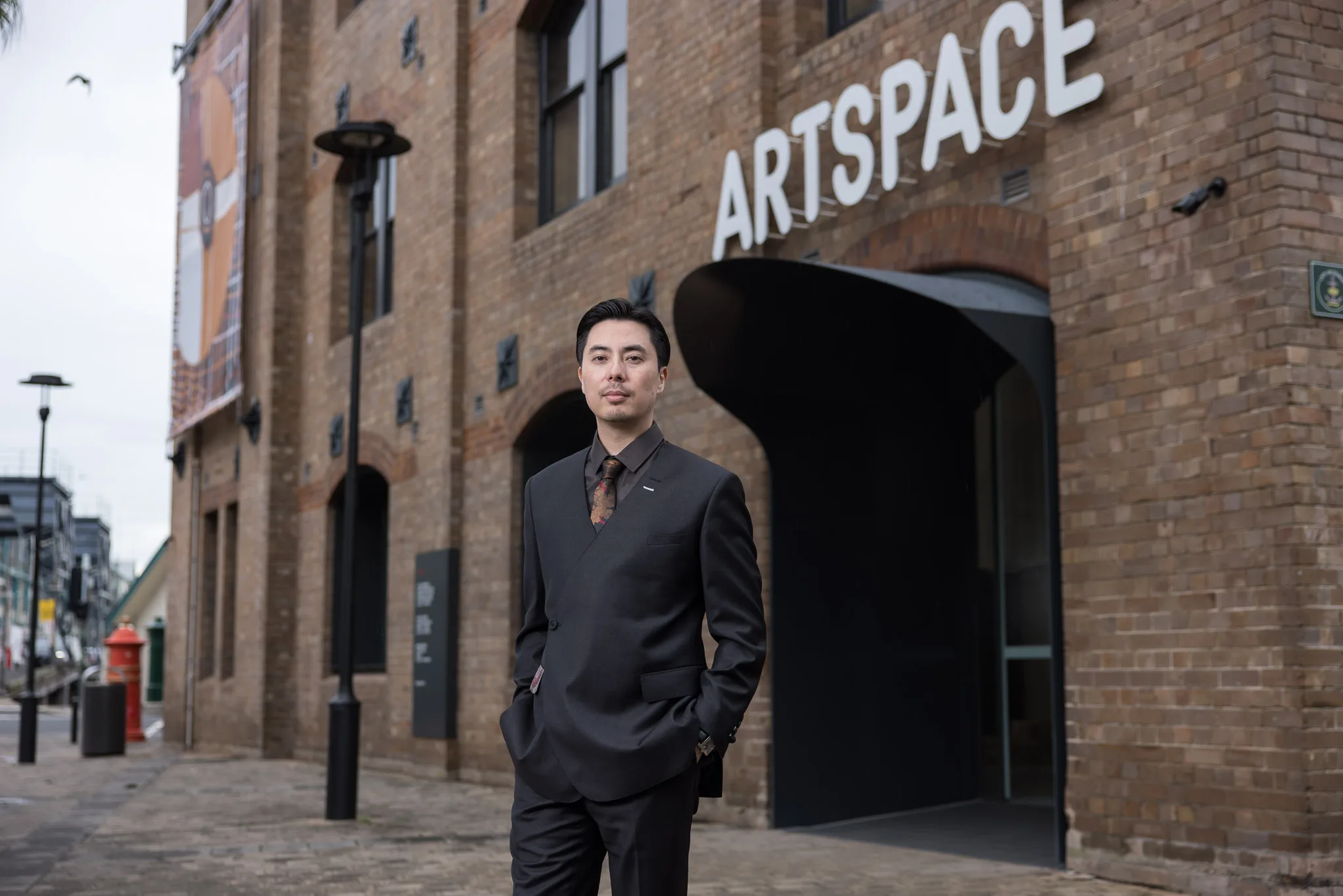 Man in dark business suit standing outside brick building with Artspace signage