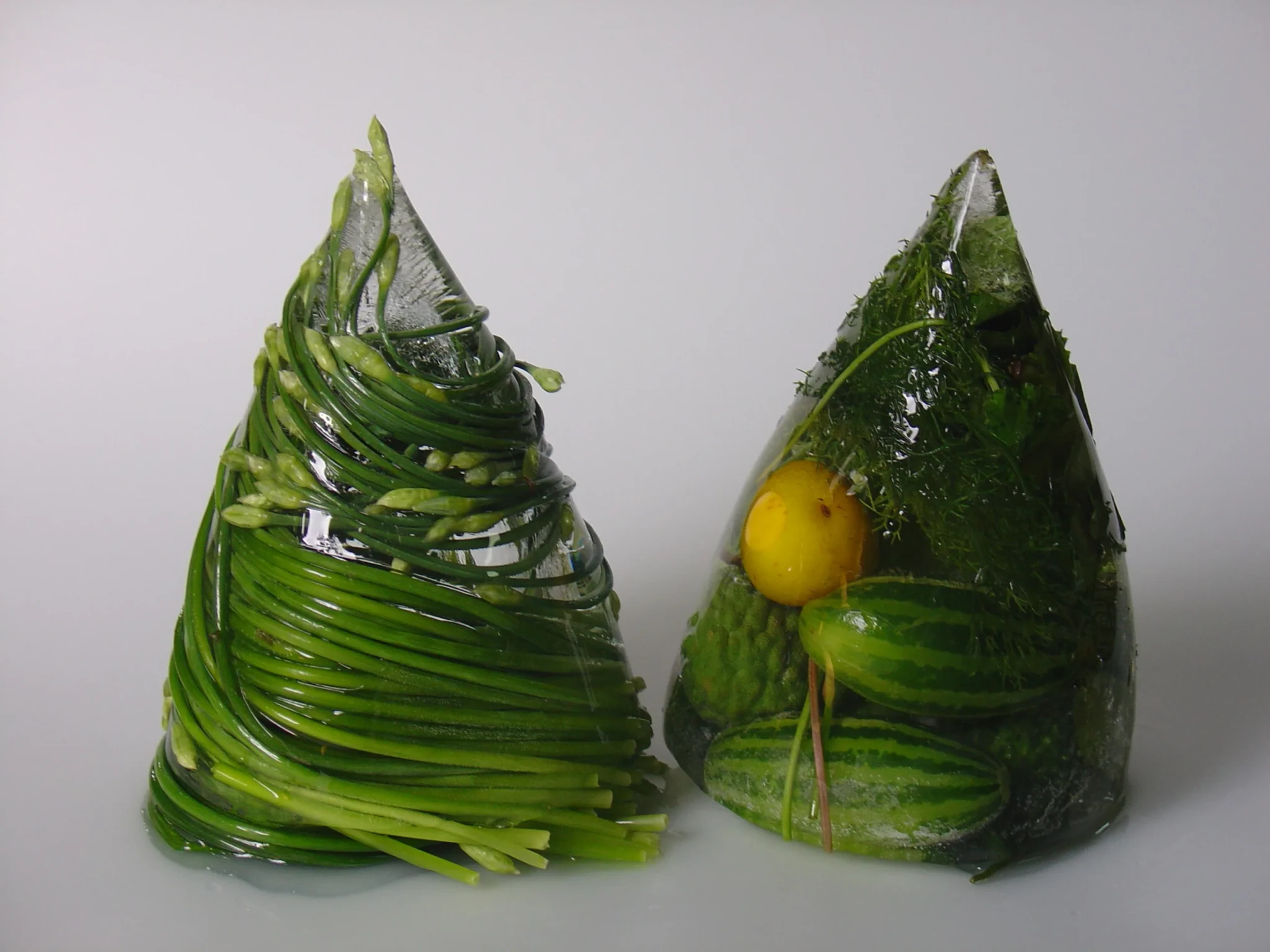 Two cone-shaped culinary sculptures made with green vegetables, herbs and contrasting elements