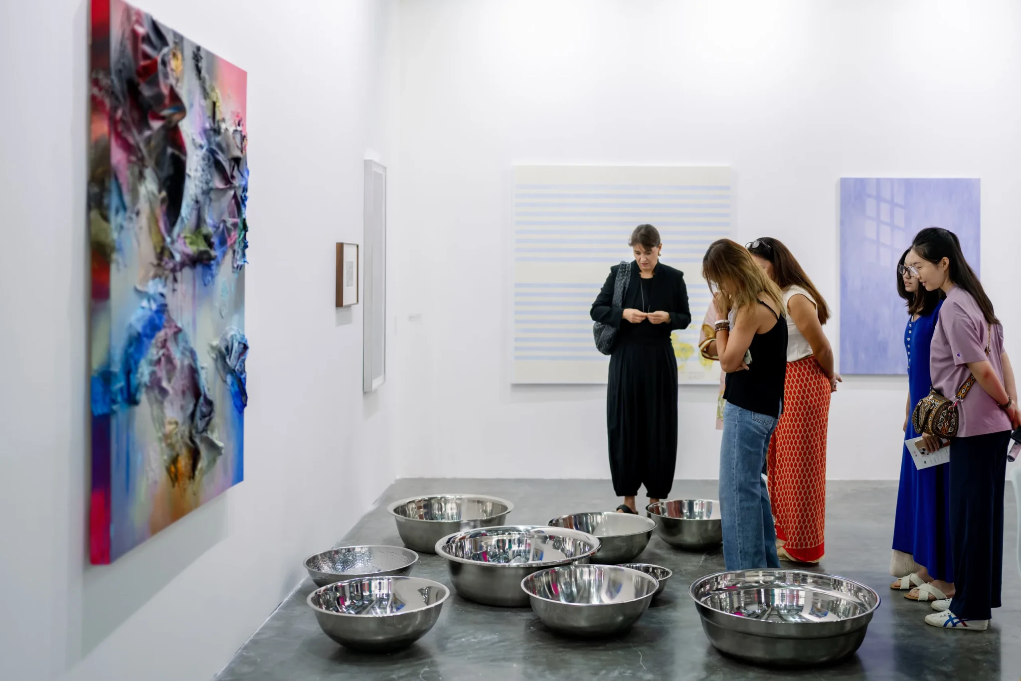 Gallery visitors viewing an art installation with metal bowls and abstract paintings