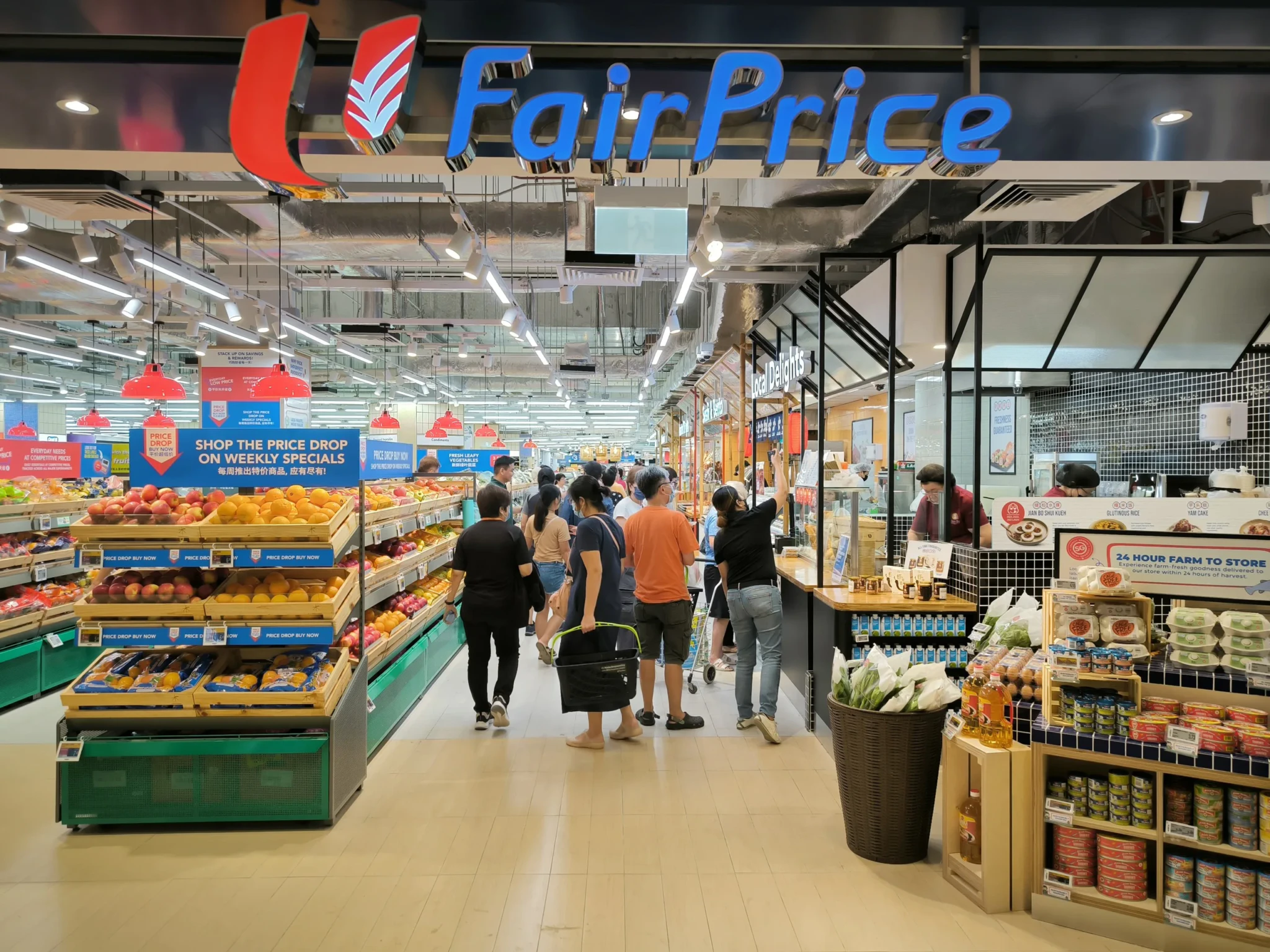 Customers shopping in a FairPrice Supermarket beside fresh produce displays and weekly specials signage