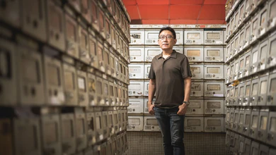 Festival Director Yong Shu Hoong standing in a corridor lined with mailboxes beneath a red ceiling
