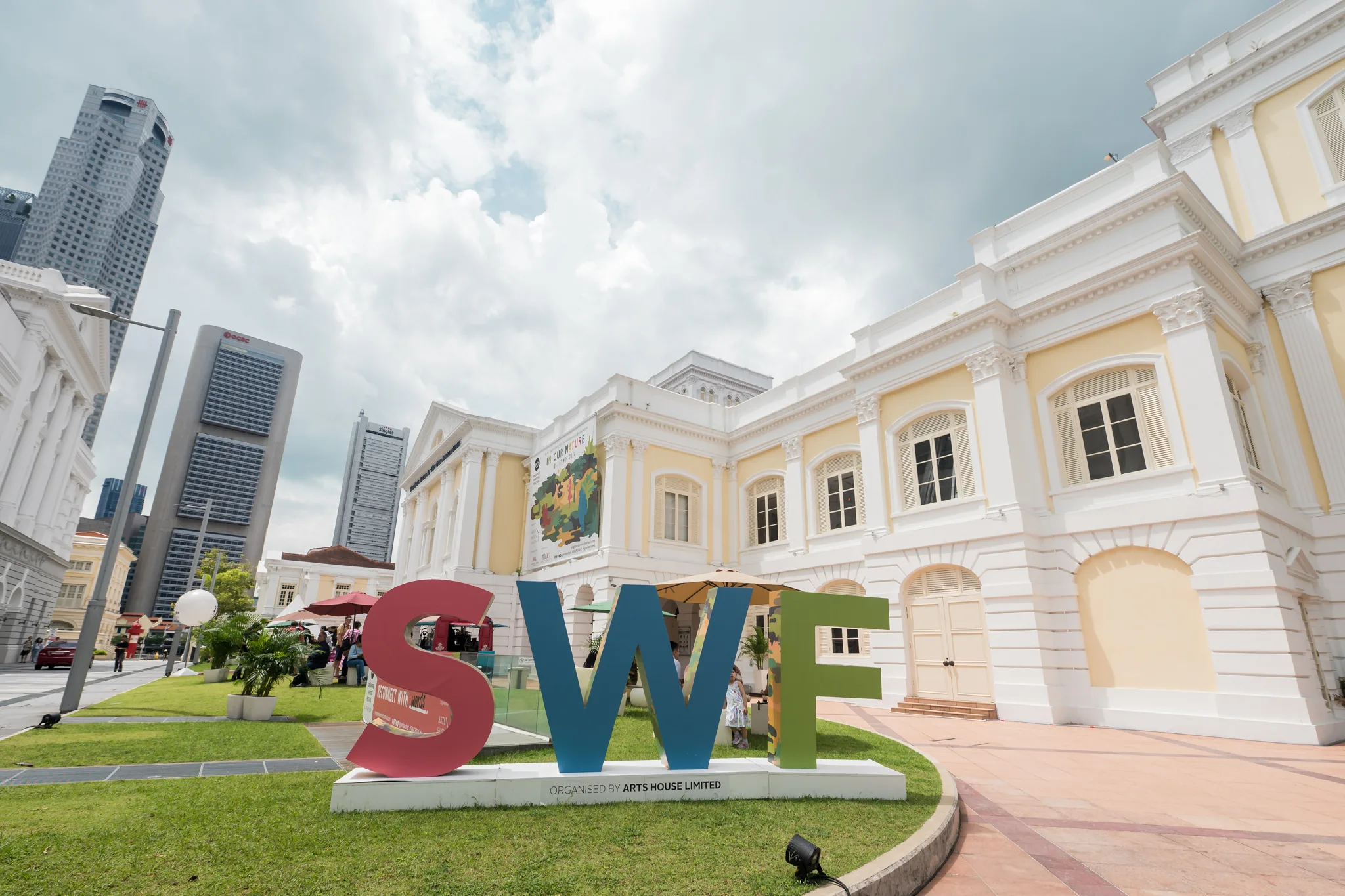Large red, blue and green SWF letters on a grass lawn, with a classical heritage building behind and city skyline