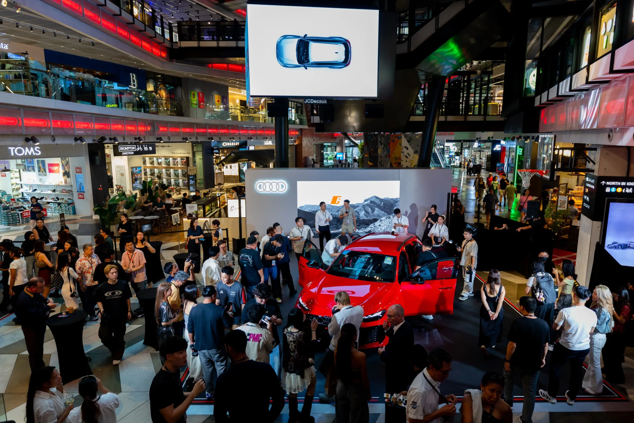 A red Audi sports car on display at Funan's atrium, with a large screen showing the car from above and visitors gathered around