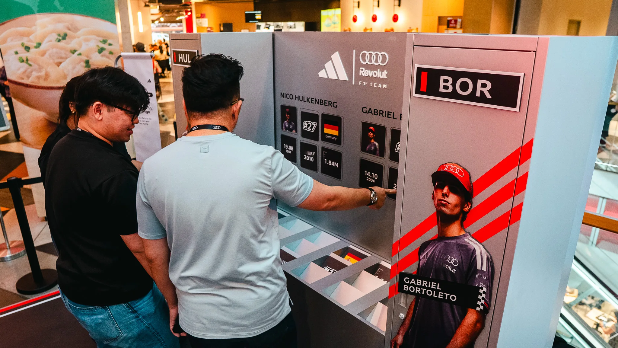 Two people at an interactive display showing Audi Revolut F1 Team driver Gabriel Bortoleto's career statistics and image