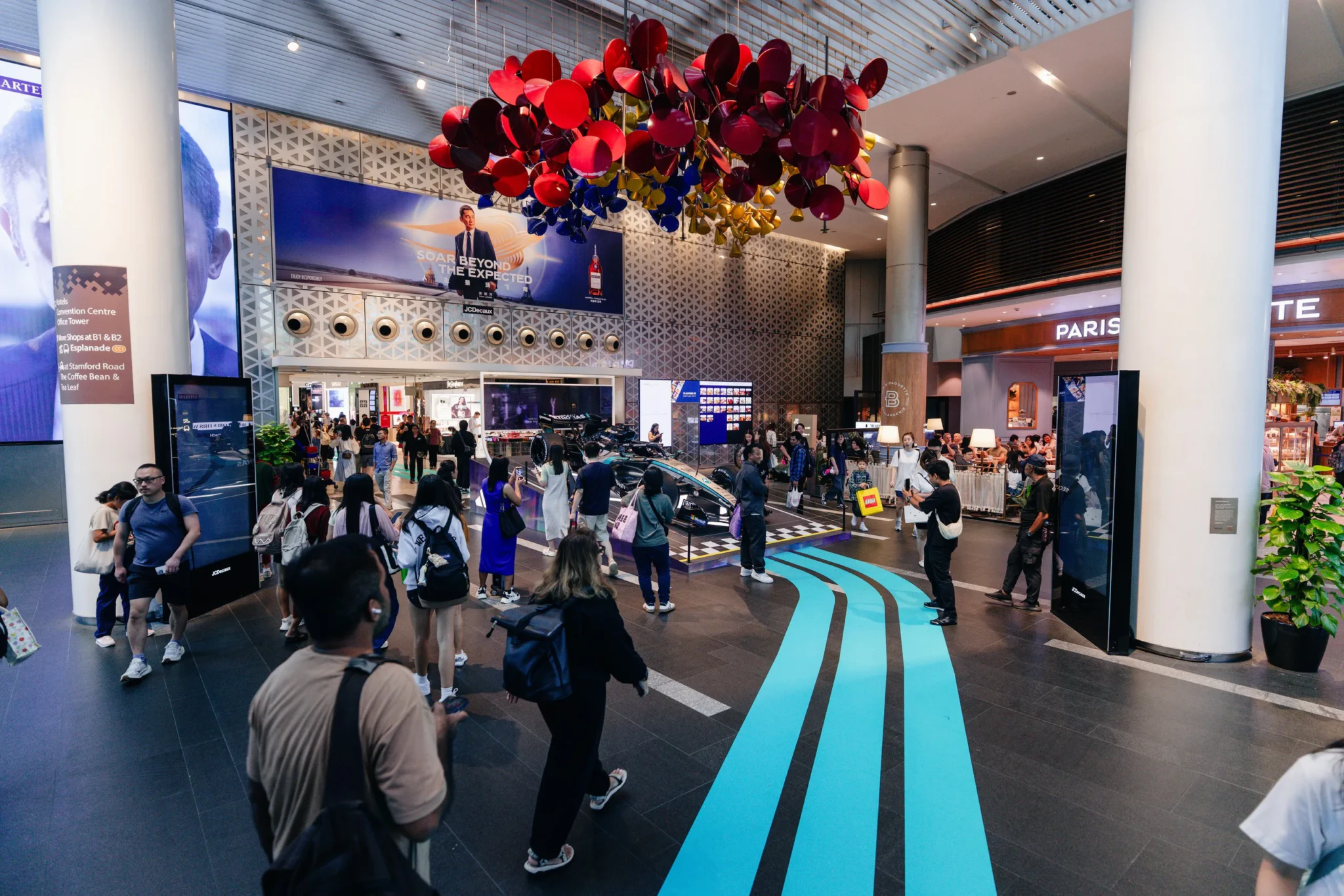 The adidas x Mercedes-AMG PETRONAS F1 Team Pop-up at Raffles City, with a red and burgundy floral installation hanging above a turquoise-lined atrium floor