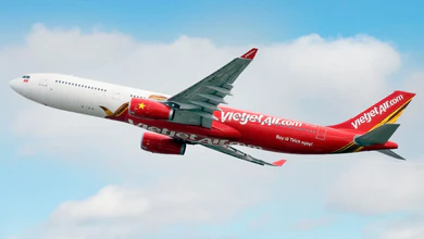 A Vietjet aircraft with a red fuselage and green tail fin flying against a blue sky with white clouds