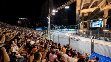 Spectators watching Formula 1 racing from Marina Bay Grandstand at night, with racing cars on illuminated street circuit