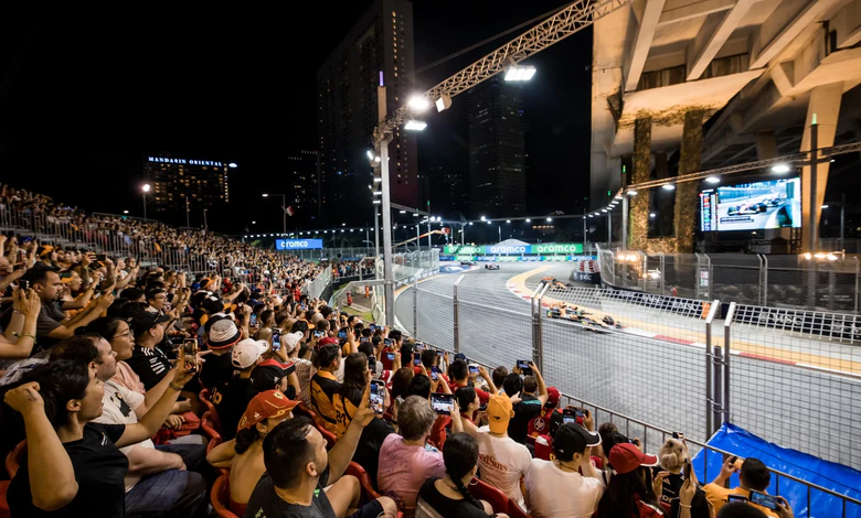 Spectators watching Formula 1 racing from Marina Bay Grandstand at night, with racing cars on illuminated street circuit