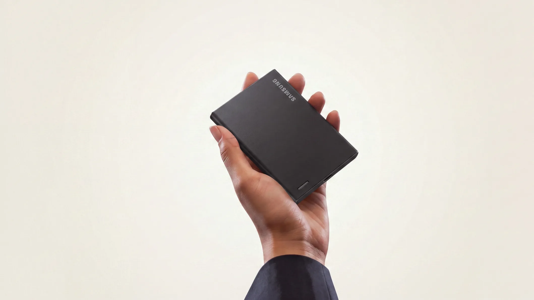 Hand holding a black Samsung portable SSD against a beige background