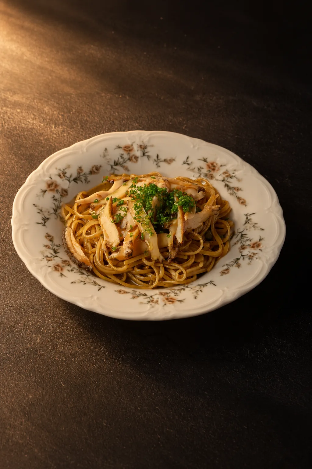 Sliced grilled abalone on noodles with fresh herbs, served on a decorative porcelain plate at Scott's Grill