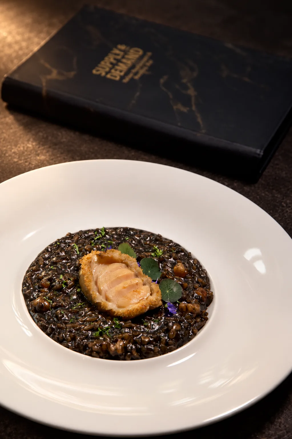 Abagold abalone on a dark risotto with microgreens and edible flowers at Supply & Demand