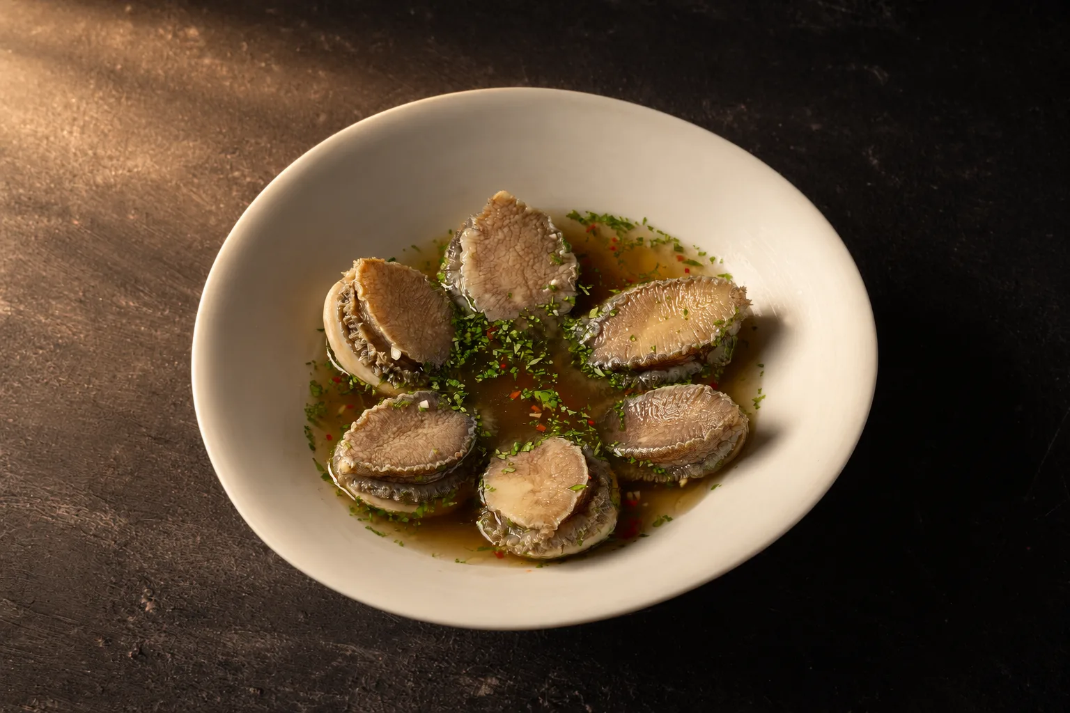 XIAN's Teochew Marinated Abalone with fresh herbs in a light broth on a white plate