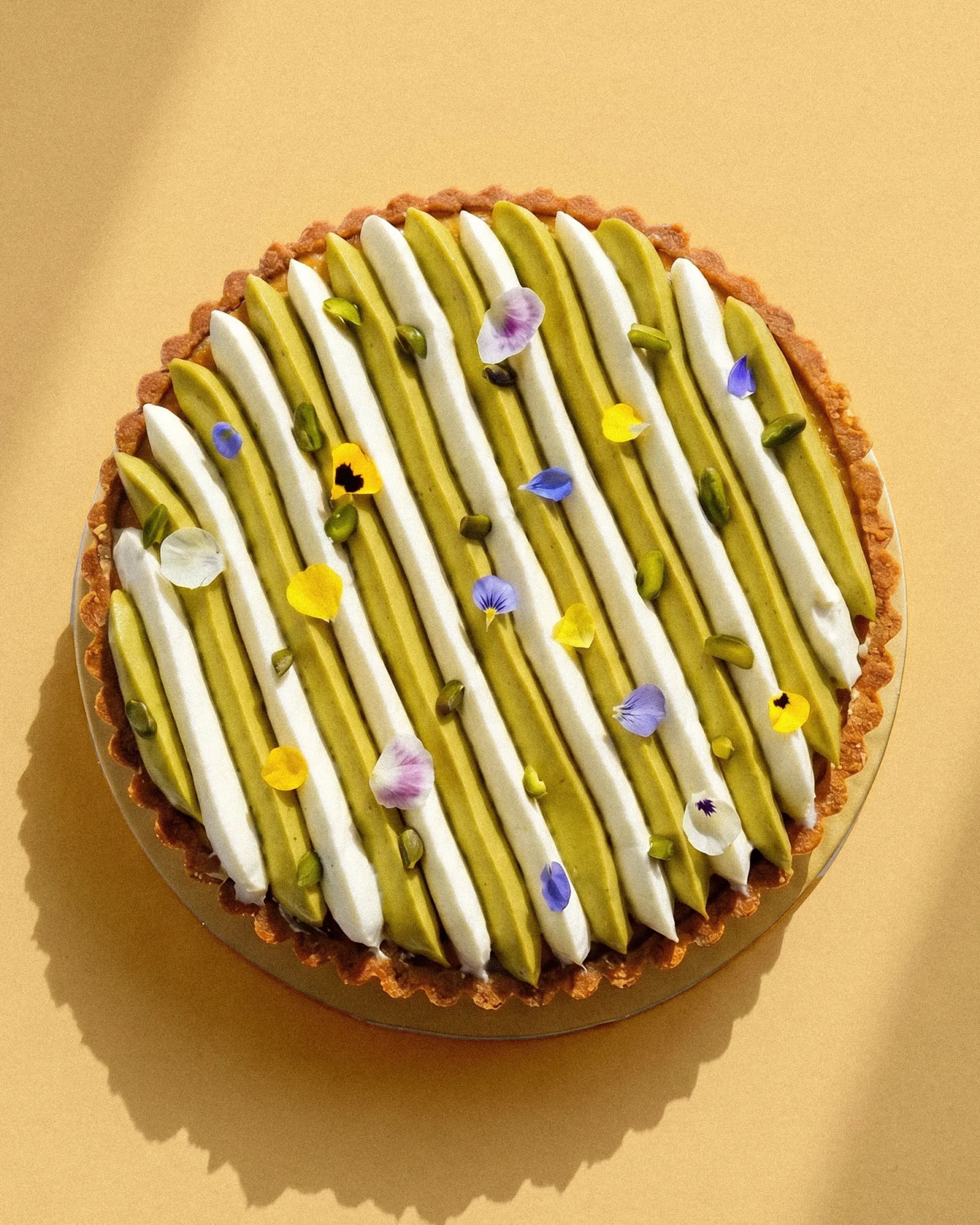 Vanilla Pistachio Cheesecake with stripes of pistachio and cream filling, candied pistachios, and edible flowers on a pastry crust